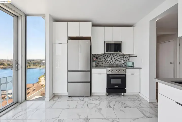 Kitchen featuring appliances with stainless steel finishes, white cabinetry, a water view, backsplash, and a wall of windows