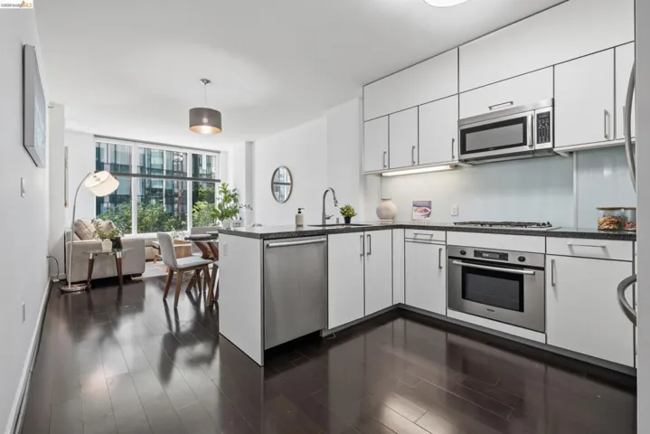 Contemporary kitchen with white cabinetry and stainless steel appliances, dark stone countertops, light blue backsplash, and wood-finish flooring