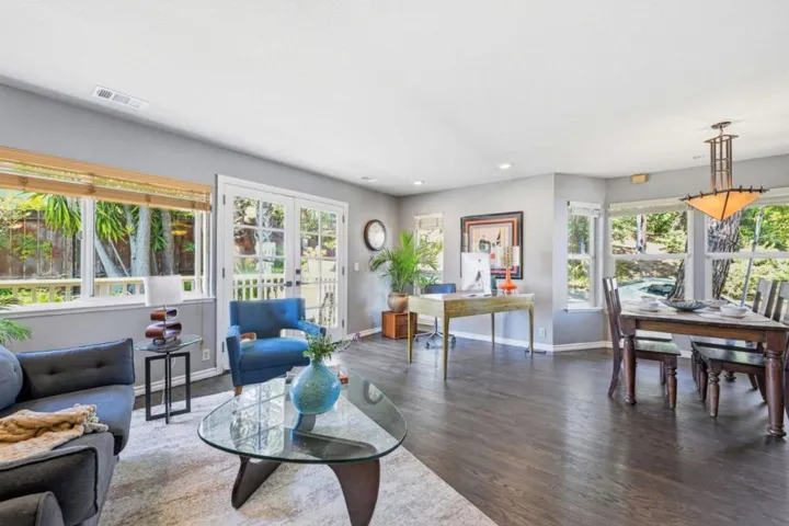 Living/dining area with corner office space next to French doors leading to outdoor deck.