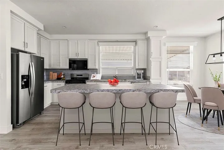 Kitchen: Open island kitchen with white cabinetry, stainless steel appliances, bar seating, recessed lighting, and seamless flow to the living and dining areas.