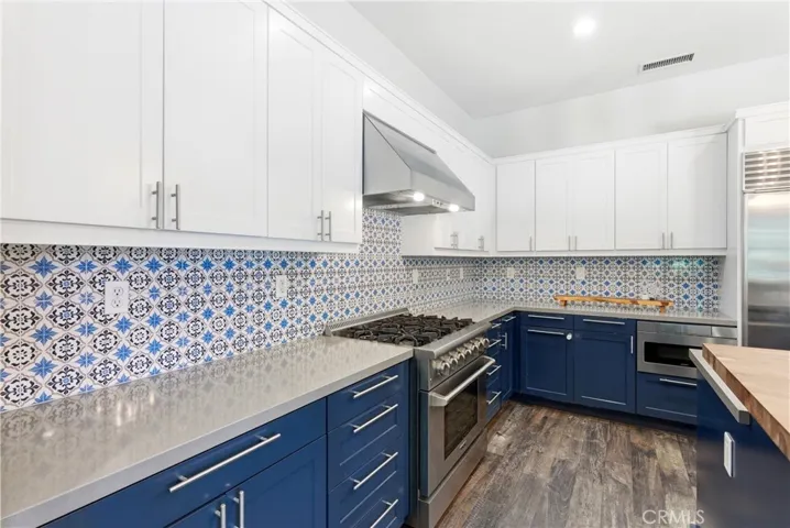 Designer kitchen with custom patterned tile backsplash, quartz counters, six-burner gas range, stainless steel hood, and modern shaker cabinetry.