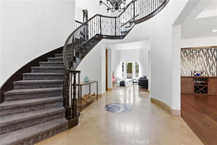 Grand foyer entrance with sweeping curved staircase, wrought iron balusters, soaring ceilings, travertine flooring, and elegant transitional design.