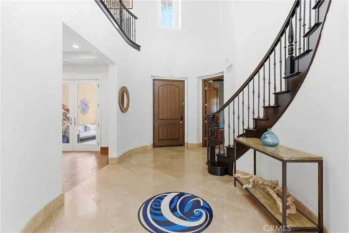 Elegant entry hall with curved staircase, travertine floors, custom iron railing, oversized front door, and dramatic double-height ceilings.