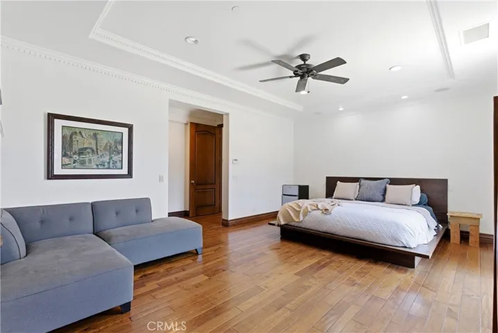 Spacious primary suite retreat featuring hardwood flooring, crown molding, recessed lighting, ceiling fan, and a dedicated sitting area creating a private lounge-like atmosphere.