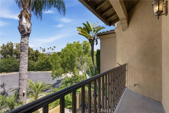 Private upper-level balcony overlooking mature landscaping, palm trees, and neighborhood views.