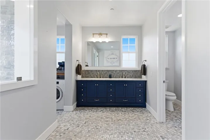 Primary bathroom vanity area showcasing custom blue cabinetry, dual sinks, designer tile backsplash, separate water closet, and spa-inspired finishes.