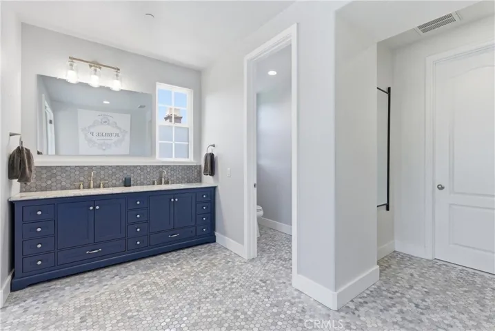 Expansive primary bathroom with oversized dual-sink navy vanity, marble-style countertops, designer hexagon tile flooring, and abundant storage.