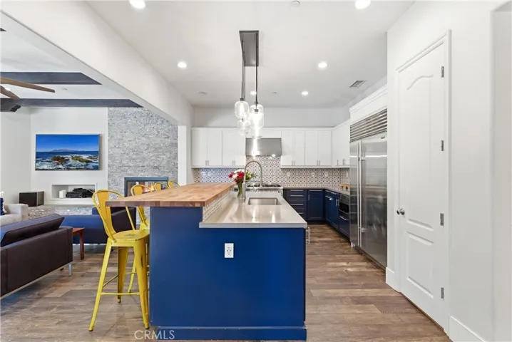 Remodeled chef’s kitchen with oversized butcher block island, custom blue cabinetry, designer pendant lighting, stainless steel appliances, and extensive counter seating.