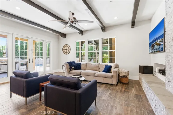 Fully remodeled family room with exposed beam ceilings, stacked-stone fireplace, wide-plank flooring, oversized windows, and indoor-outdoor living access.