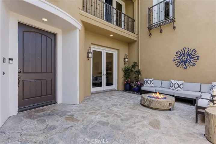 Private front courtyard entry with natural stone flooring, outdoor lounge seating, gas fire feature, covered patio, and French doors creating seamless indoor-outdoor flow.