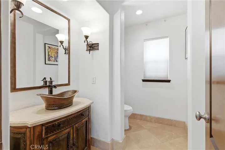 Custom powder room with furniture-style vanity, vessel sink, stone countertop, designer lighting, and travertine flooring.