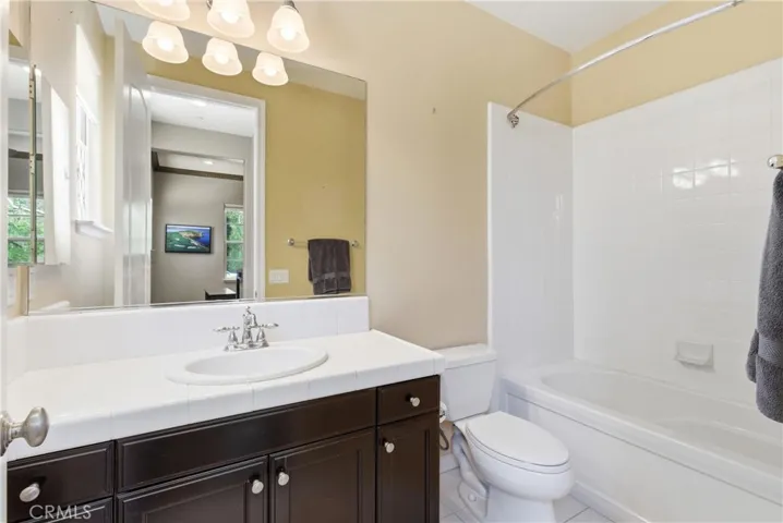 Main level guest bathroom featuring a tub and shower combination, oversized vanity mirror, and neutral finishes adjacent to the downstairs bedroom.