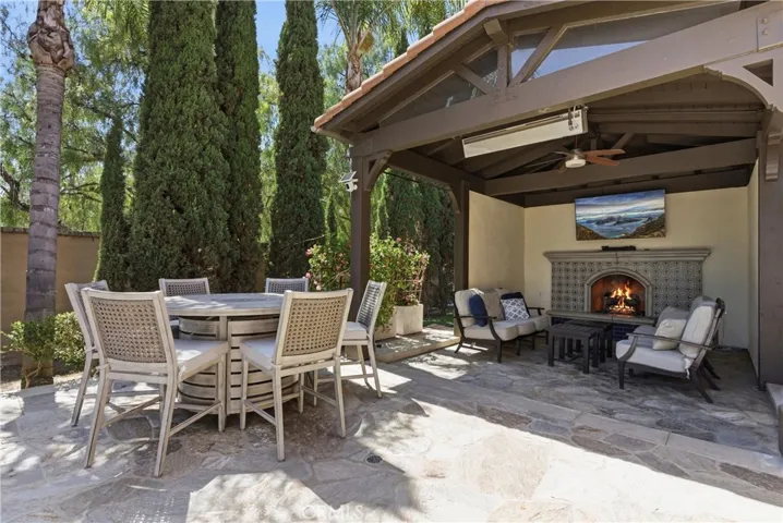 Covered outdoor lounge pavilion with custom fireplace, mounted TV, ceiling fan, and built-in heaters