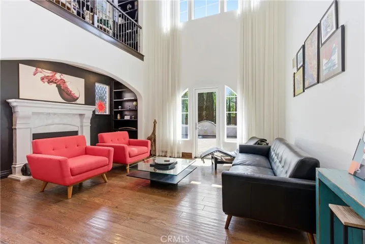 Dramatic two-story living room with floor-to-ceiling windows, abundant natural light, custom drapery, hardwood flooring, and statement fireplace.