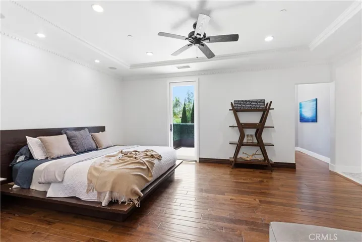 Expansive primary suite with hardwood flooring, fireplace retreat, oversized proportions, and private balcony access overlooking lush greenery and hillside views.