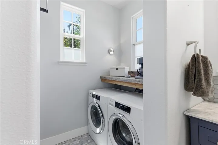 Spacious upstairs laundry room with side-by-side washer and dryer, natural light, custom countertop workspace, and adjacent dual-vanity bath with designer​​‌​​​​‌​​‌‌​​‌​​​‌‌​​​‌​​‌‌​​‌‌​​‌‌​​​​ finishes.