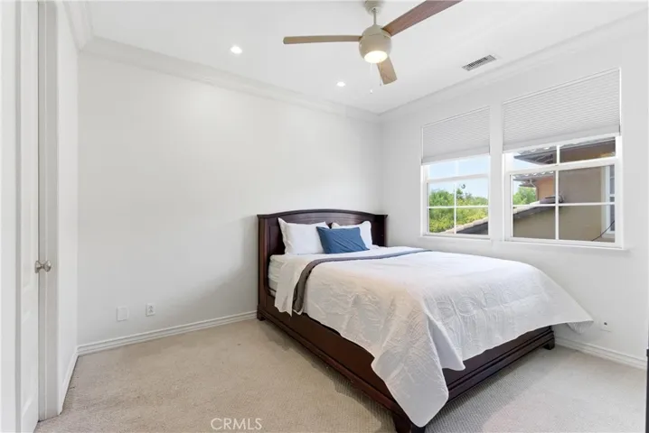 Spacious upstairs bedroom with plush carpeting, crown molding, ceiling fan, and oversized windows.