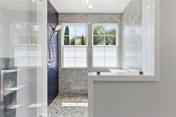 Spa-inspired primary bathroom featuring a frameless walk-in shower, designer tilework, pebble stone flooring, and abundant natural light