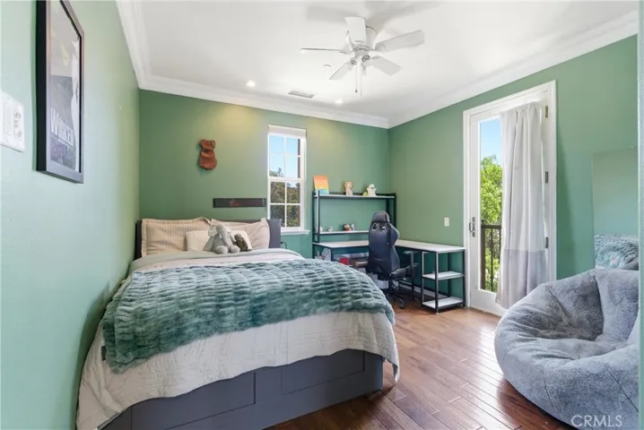 Versatile upstairs bedroom with green accent walls, hardwood flooring, study space, ceiling fan, and private balcony access.