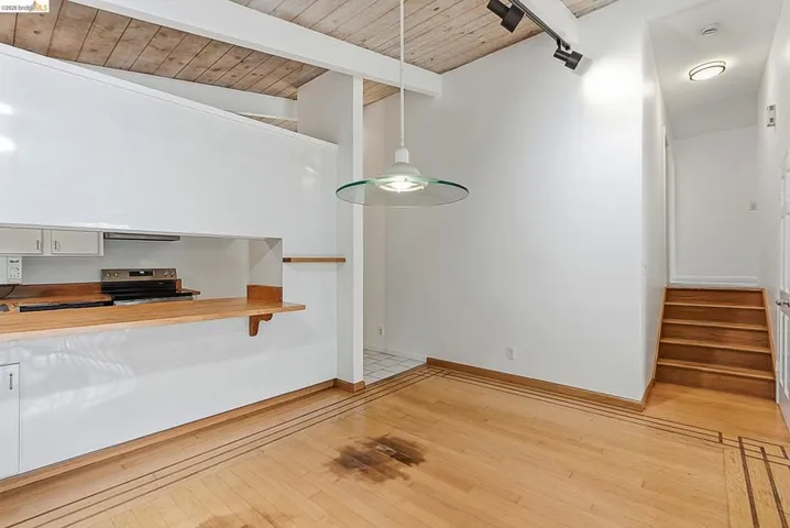 Open-concept living area featuring wood-finish flooring with decorative inlay, a pass-through kitchen counter with wood-finish surface, recessed lighting, and a staircase with wood-finish treads