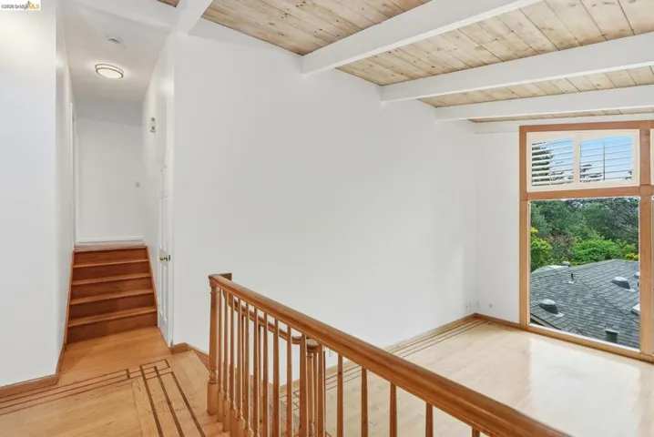 Bright open space with exposed beam ceiling, natural wood-finish flooring, and a large window