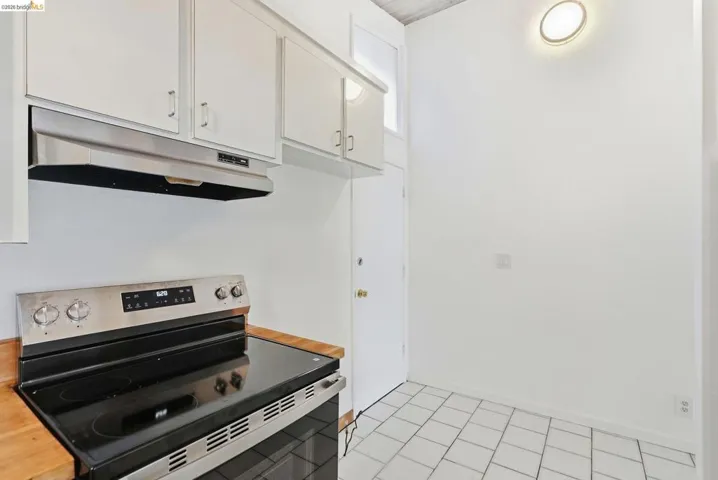 Kitchen featuring stainless steel range, coordinating stainless steel hood, white cabinetry with silver hardware, wood-finish countertops, and white square tile flooring
