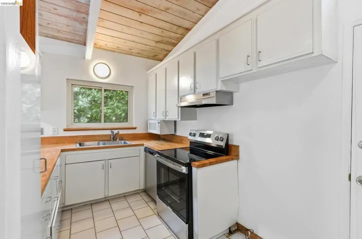 Kitchen featuring a vaulted wood-paneled ceiling, white cabinetry, wood-finish countertops, stainless steel appliances, and tiled flooring