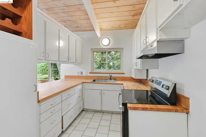 Kitchen featuring a wood-finish ceiling with exposed beams, white cabinetry, wood-finish countertops, tiled flooring, and a stainless steel sink