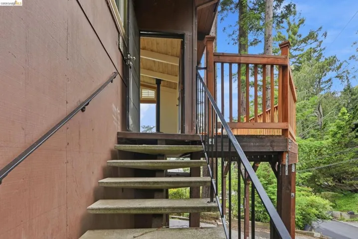 Exterior entry featuring concrete steps with metal railings, a wooden deck with a wooden railing, and a clear sky backdrop