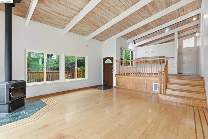 Vaulted wood-plank ceiling with exposed beams, wood-finish flooring, and a black wood-burning stove with a green stone hearth