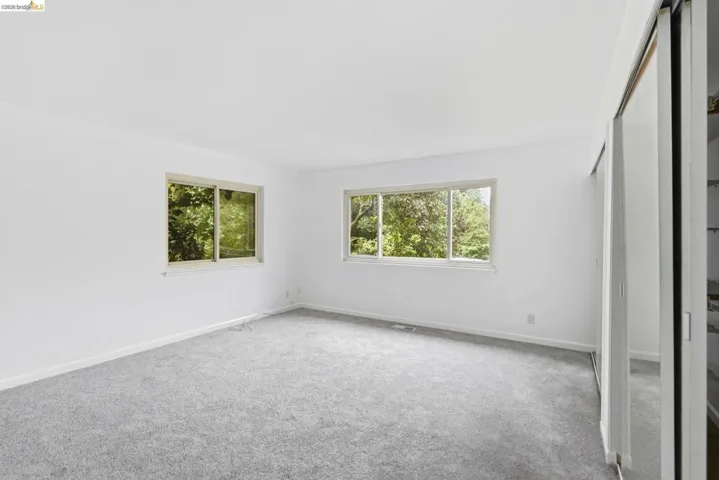 Bright room featuring two large windows, light gray carpeting, fresh white walls, and a sliding door closet with mirrored panels