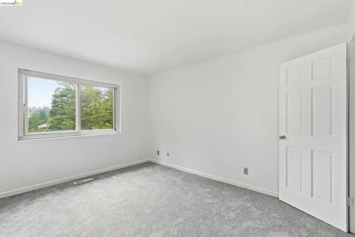 Windowed room featuring light gray carpeting, white walls, and a six-panel interior door