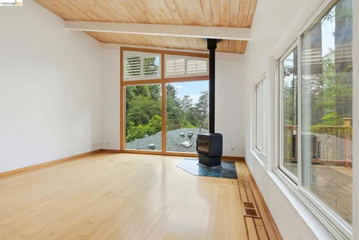 Bright interior space featuring a wood-finish vaulted ceiling with exposed beams, light wood-finish flooring, and a freestanding fireplace with a stone hearth
