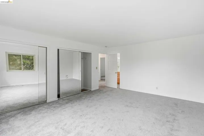 Wall-to-wall carpeting and bright white walls define this room, featuring two sliding mirrored closet doors