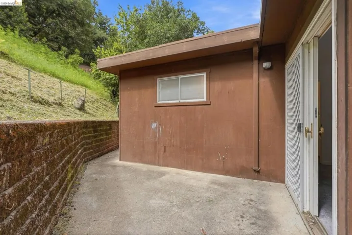 Exterior concrete patio area featuring a brown-toned retaining wall and a white security screen door