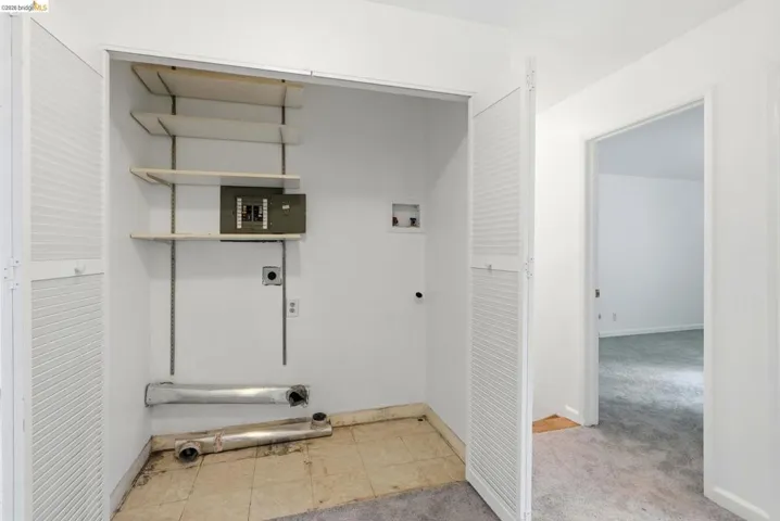 Laundry closet with louvered bi-fold doors, wall-mounted adjustable shelving, and an electrical panel