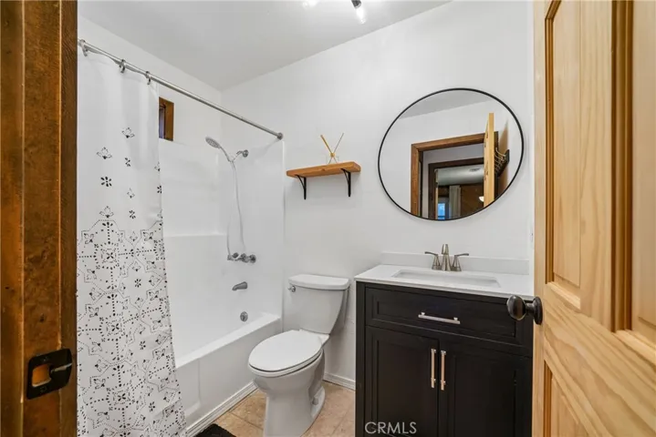Full bathroom with tub-shower combination, vanity, round mirror, and updated finishes.