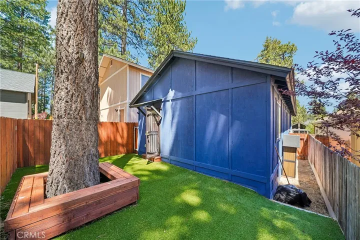Fenced backyard with turf, mature pine tree, and built-in seating area.