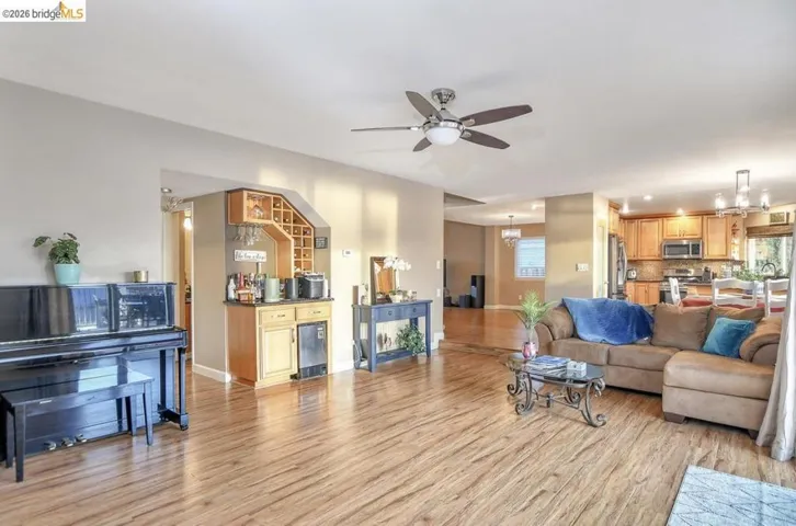 Living area featuring light wood-type flooring, a chandelier, a dry bar, and ceiling fan