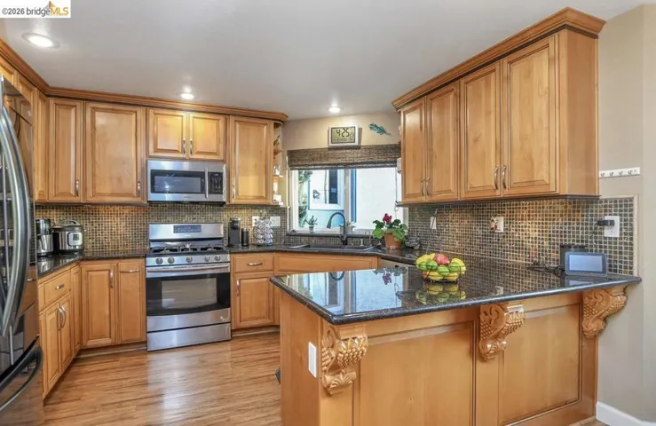 Kitchen with dark stone counters, stainless steel appliances, brown cabinetry, and recessed lighting