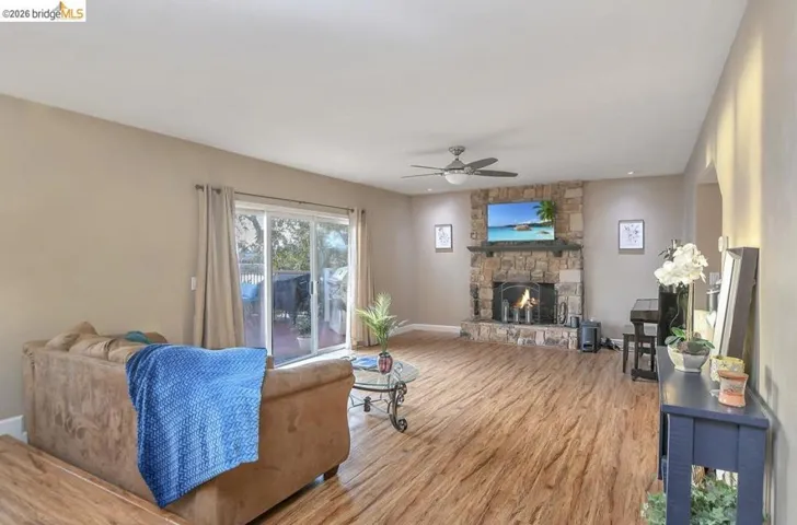 Living room featuring wood finished floors, a stone fireplace, and a ceiling fan