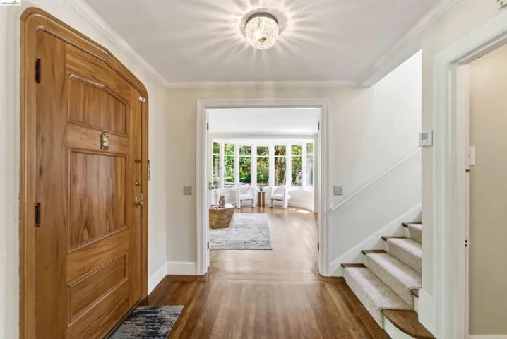 Entry foyer featuring wood-finish flooring, a detailed wood entry door, crown molding, and a crystal flush-mount light fixture