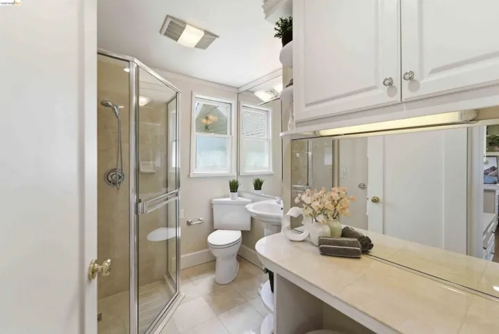 Bathroom featuring a glass-enclosed shower, pedestal sink, built-in vanity with tiled countertop, and overhead storage cabinetry