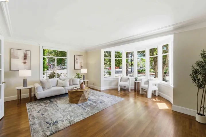 Spacious living area featuring extensive bay windows, crown molding, wood-finish flooring, and light-toned wall finishes
