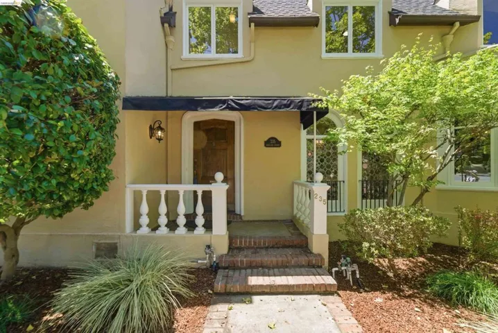 Stucco exterior with a black fabric awning over the arched entryway, featuring a prominent wrought iron outdoor light fixture and white balustrade porch railings