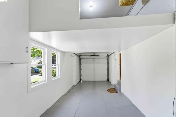Bright garage space featuring a roll-up door, two casement windows, overhead lighting, and built-in white cabinetry