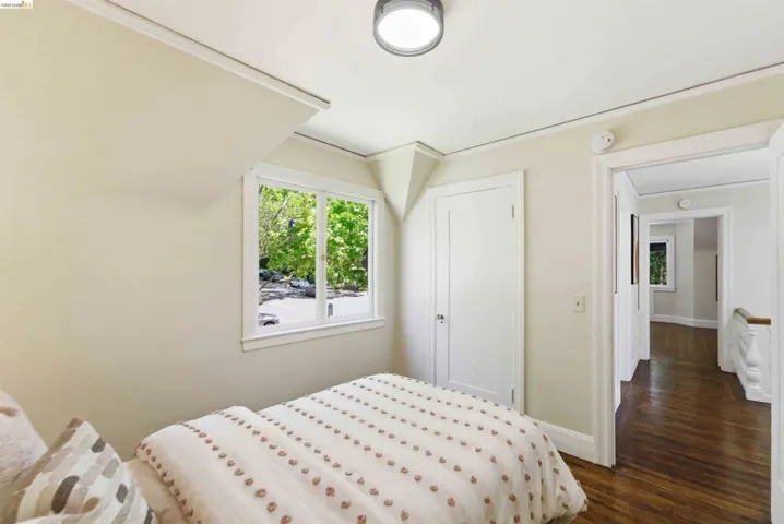 Room featuring a double-hung window, light-colored walls, a flush-mount ceiling light, a white door with a dark knob, and dark wood-finish flooring extending into the hallway