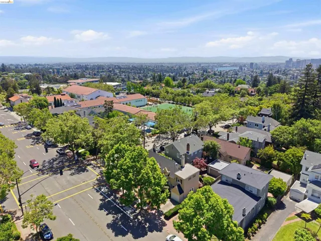 Expansive aerial perspective showcasing a residential neighborhood with mature trees, a multi-building complex with a red tile roof, and a distant cityscape with a body of water
