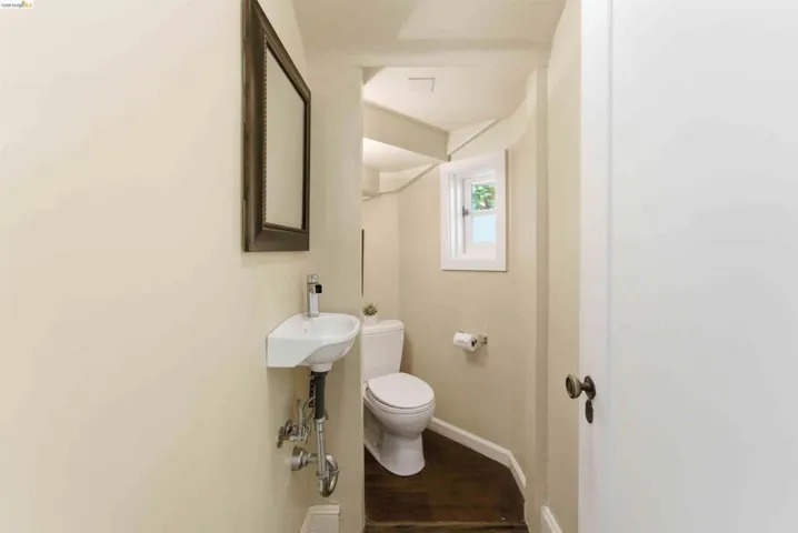 Compact powder room featuring a wall-mounted sink, a toilet, a framed wall mirror, and a small window for natural light