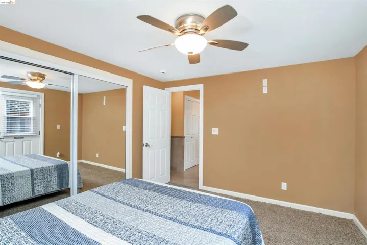 Bedroom featuring a ceiling fan with integrated lighting, mirrored closet doors, and neutral carpeting